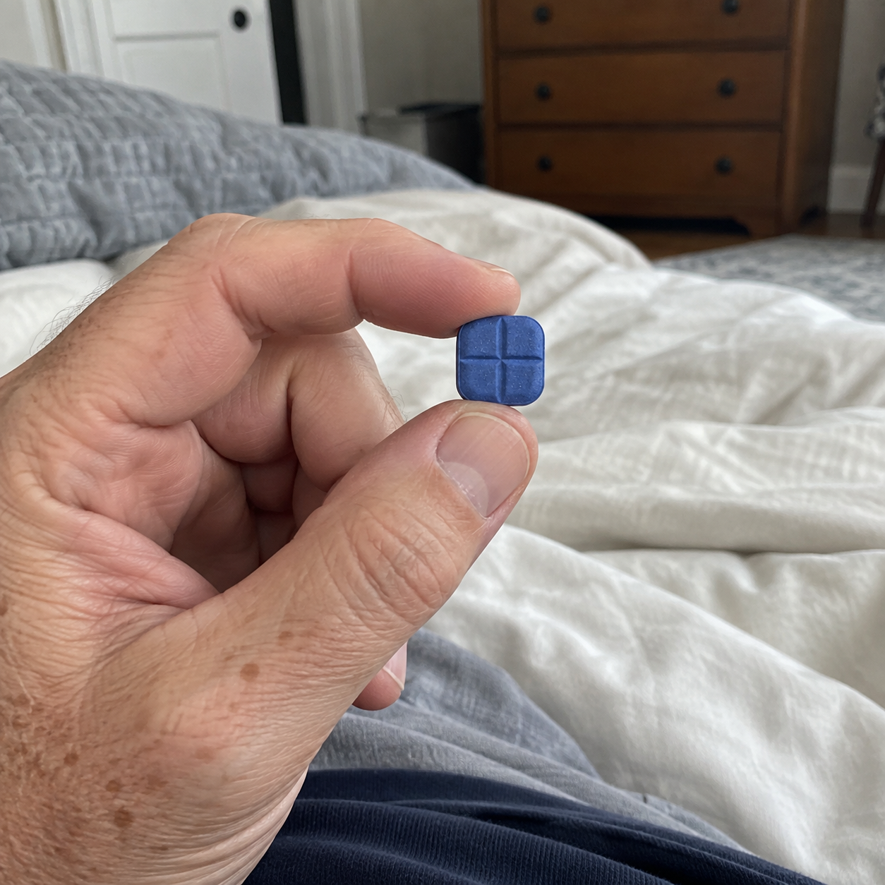 A man holding a small blue cross-scored tablet between his fingers