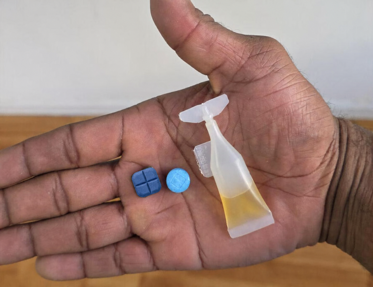 Open palm holding a square blue tablet, a round blue tablet and a liquid ampoule